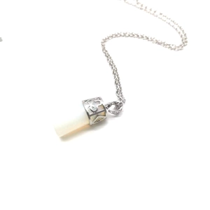 Macro detail of cylindrical white stone pendant with silver filigree engraving on top