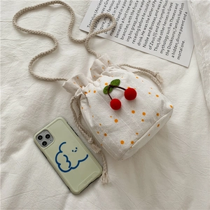 Close-up of a small white canvas bucket bag with daisy embroidery and cherry pendant