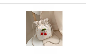 Detail of a white drawstring bucket bag with yellow dots and cherry embroidery