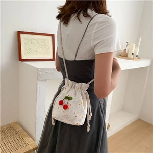 Detail view of canvas bucket bag with cherry embroidery and drawstring strap on a model