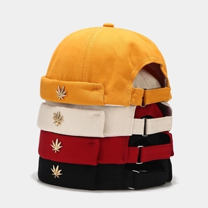 Detail of four colorful brimless docker hats with canvas texture and metal leaf badges