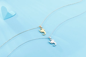 Close-up of gold and silver scorpion pendant necklaces on a light blue background