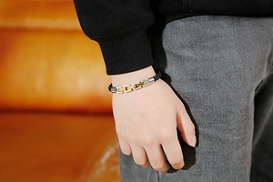 Close-up of a men's black braided leather bracelet with gold and silver metal accents