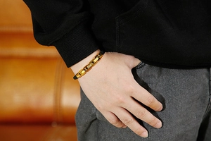 Close-up of golden stainless steel chain and black braided leather bracelet on wrist
