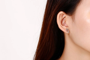 Close-up of minimalist silver fish-shaped stud earrings worn by a model in a studio shot
