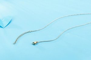 Detail of the golden necklace lobster clasp and extender chain on a blue background