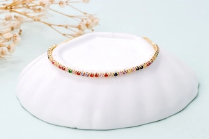 Detail of colorful rainbow tennis bracelet with gold chain on a textured shell plate