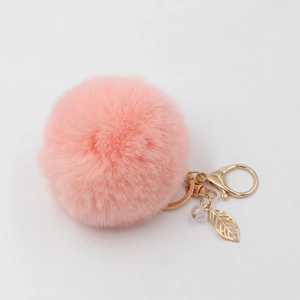 Portachiavi con pompon rosa, ciondolo a foglia dorata e perla su sfondo bianco