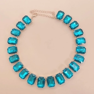 Detailed close-up of aquamarine rectangular crystal necklace on a soft pink background