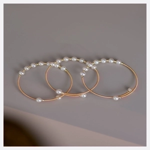 Three-piece gold-toned metal bangles with white pearls and elegant woven design