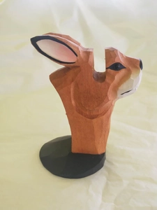 Close-up of hand-carved wooden rabbit eyeglass holder with natural grain on a round base