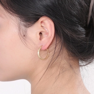 Close-up of gold plated stainless steel hoop earrings with diamond-cut texture on model