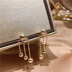 Elegant gold long tassel earrings with metallic balls on a luxury jewelry box display