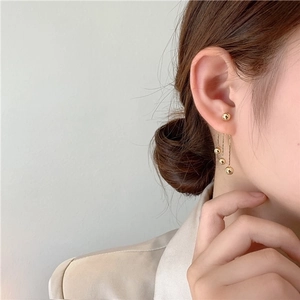Detail of elegant gold long tassel earrings with spherical studs on model ear