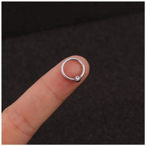 Polished stainless steel piercing ring with round clear zircon held on a fingertip