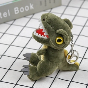 Close-up of a green plush T-Rex dinosaur keychain with metal ring on checkered fabric