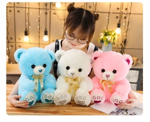Three plush teddy bears in blue, white, and pink with shiny details and gold ribbons