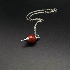 Macro shot of silver pendulum necklace with a polished red stone and metallic cone