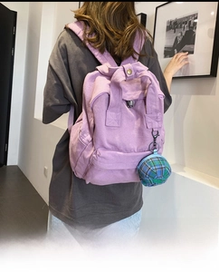 Detail view of purple canvas backpack with a mini plaid hat charm and secure zipper pocket