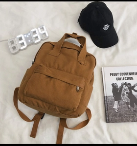 Close-up of brown canvas backpack with large front zip pocket on a white bed