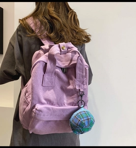Detail showing a purple canvas backpack with a plaid coin purse accessory on a model