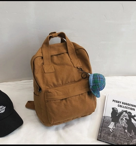 Brown canvas backpack with green plaid mini cap pendant and adjustable straps