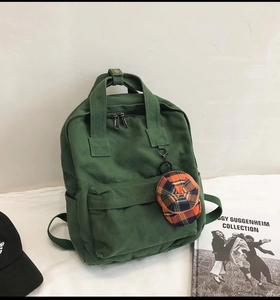 Detail of dark green canvas backpack with adjustable straps and mini baseball cap keychain