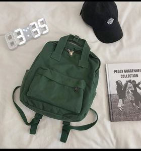 Detailed view of a green canvas backpack featuring front zipper pocket and adjustable straps
