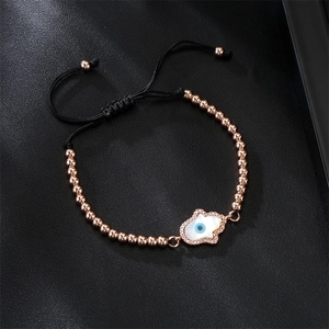 Close-up of rose gold Hamsa hand bracelet with blue evil eye on black leather