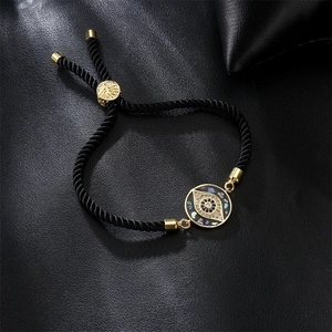 Detailed close-up of a golden evil eye charm on an adjustable black woven cord bracelet