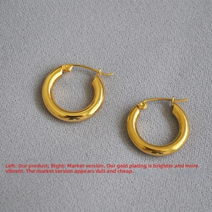 Close-up of thick gold-plated hoop earrings with a high-shine mirror finish on grey fabric