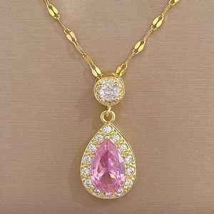 Macro shot of gold teardrop necklace with pink gem and white zircon pavé setting