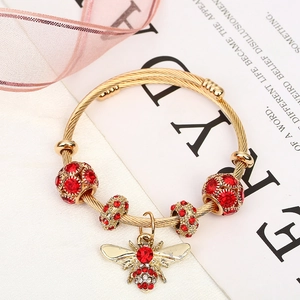 Golden spiral cuff bracelet featuring red rhinestone beads and a sparkling bee pendant