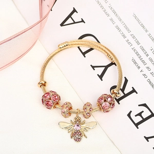 Macro detail of golden twist bracelet featuring pink crystal beads and a honey bee charm