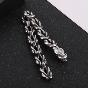 Macro shot of silver stainless steel dragon scale braided chain bracelet on dark surface