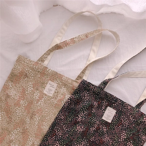 Detailed texture of lightweight cotton floral tote bags in beige and black variants
