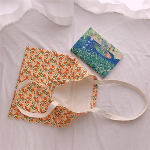 Flat lay of cream cotton shoulder bag with orange fruit pattern on white fabric