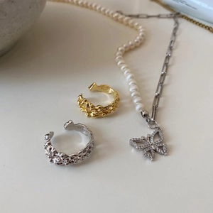 Macro shot of 925 silver lava rings and pearl butterfly necklace on white table