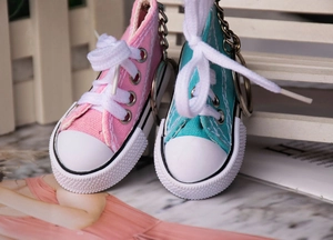 Close-up of mini canvas shoe keychains in pink and blue with white laces and metal rings