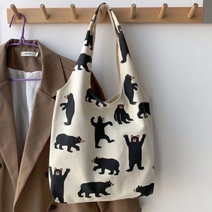 Detail of cream canvas tote bag with black bear print hanging on a wooden rack