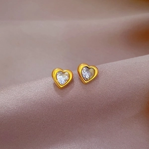 Macro view of gold-tone heart stud earrings with sparkling white crystals on purple silk