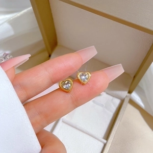 Golden heart earrings with zircon inlay held on hand against white silk background