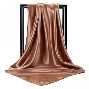 Detailed view of glossy bronze satin square scarf draped over a black display frame