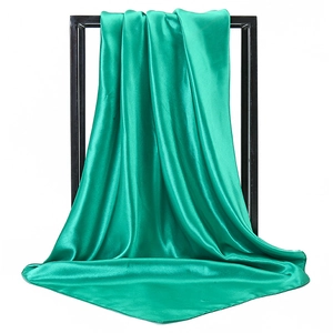 Elegant emerald green satin square scarf draped on a black minimalist rack detail