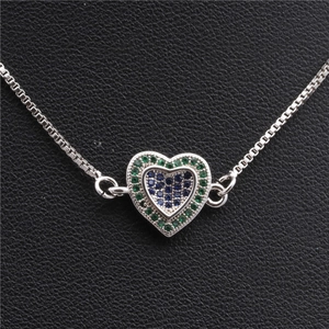 Détail macro du collier cœur argenté avec zircons bleus et verts sur cuir noir
