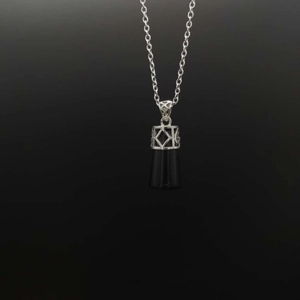 Macro shot of black cylindrical stone pendant with ornate silver geometric cutout clasp