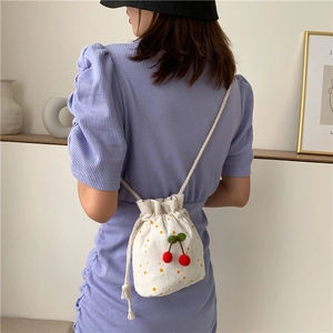 Detailed back view of a white canvas bucket bag with cherry charms and yellow dots