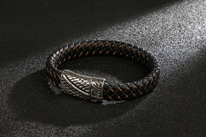 Close-up of a woven leather bracelet featuring a silver metal buckle with feather relief