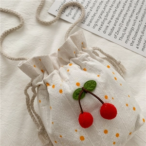 Detail of white floral canvas bucket bag with plush cherry decor and woven strap