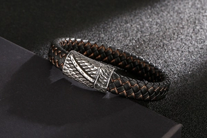 Detail of woven black leather bracelet with metal feather clasp on grey background